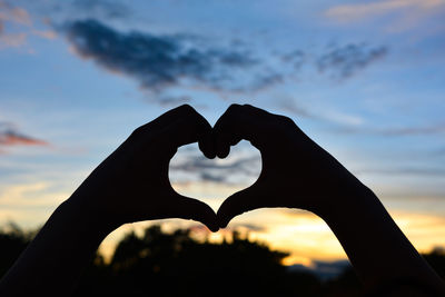 Silhouette hand holding heart shape against sky during sunset