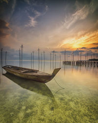 Sailboats moored on sea against sky during sunset