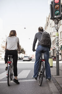 Rear view of couple with bicycles waiting on signals at city street