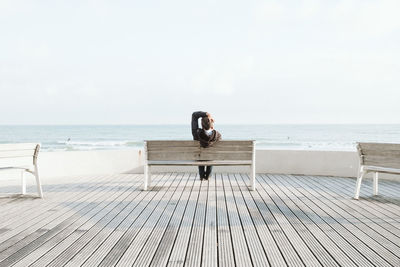 Man sitting on wood at beach against sky