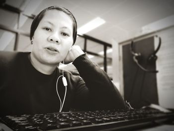 Portrait of woman with in-ear headphones sitting with computer keyboard