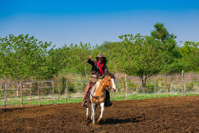 Cowboy riding horse at ranch on sunny day