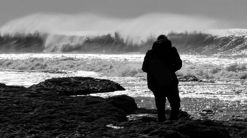 Rear view of silhouette man standing on rock formations in front of sea