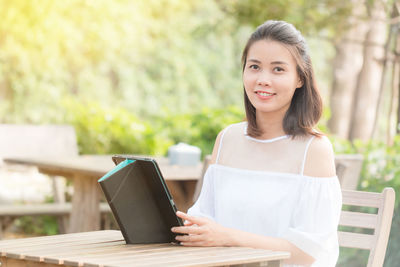 Portrait of smiling young woman using digital tablet at sidewalk cafe