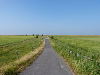 Empty road amidst field against clear sky