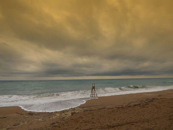 Lifeguard watchtower at sea shore against storm cloud during sunset