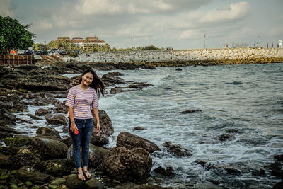 Man standing on rock by sea against sky