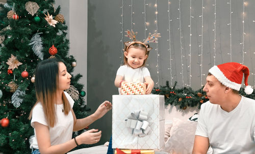 Side view of young woman using digital tablet while standing by christmas tree at home