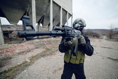 Army soldier aiming while standing against built structure