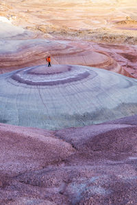 High angle of traveler in outerwear with backpack standing on top of smooth stone formation while exploring bentonite hills in utah, usa