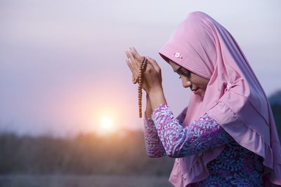 Midsection of woman with pink umbrella against sky during sunset