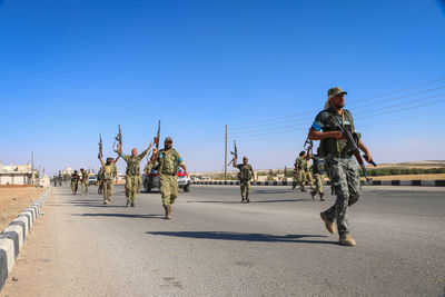 People walking on road against clear blue sky