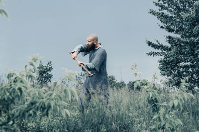 Emotional photo of medieval viking in metal chain mail swinging ax. background of green grass