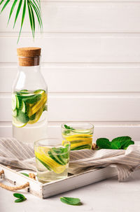 Sassy water for detox infused with lemon, cucumber and mint in glasses at white wooden tray. 