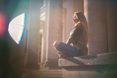 Woman sitting on built structure in sunny day