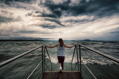 Rear view of woman moving down on pier in sea against cloudy sky