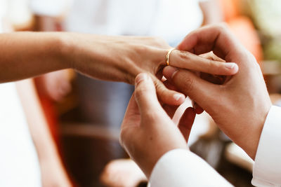 Cropped hands of groom wearing wedding ring to bride