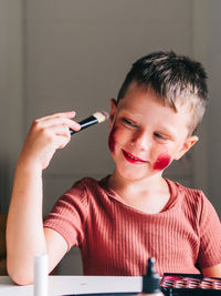 Charming child with makeup applicator looking away at table with eyeshadow palette