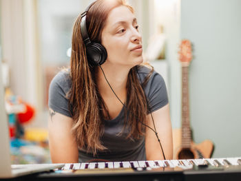 Smiling woman wearing headphones sitting by piano at home