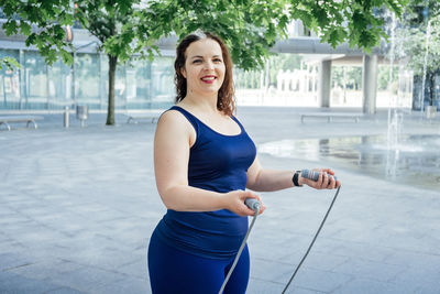 Confident plus size curvy happy young woman doing exercise workout with skipping rope outdoors.