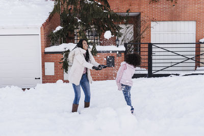 Mother and daughter playing with snow outside house during winter