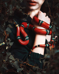 Midsection of woman with snake on hand amidst plants