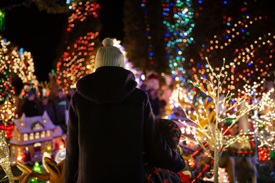 Rear view of people standing against illuminated christmas lights at night