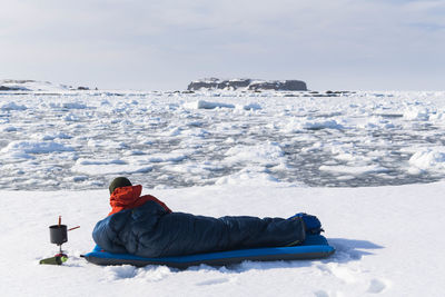 Male hiker resting in sleeping bag on snow covered land