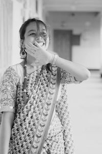 Smiling young woman looking away while standing in corridor