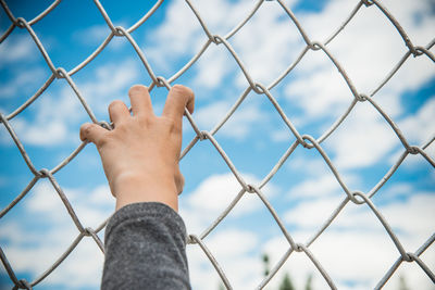 Low section of man standing on chainlink fence against cloudy sky