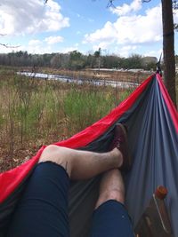 Low section of person relaxing on tent against sky