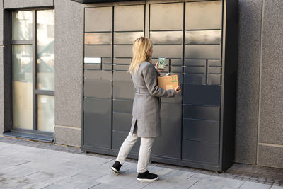 Beautiful woman picking up a package from a smart electronic steel parcel locker box, automatic