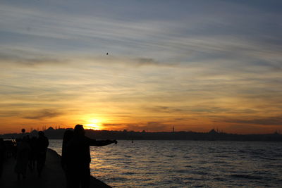 Silhouette man by sea against sky during sunset