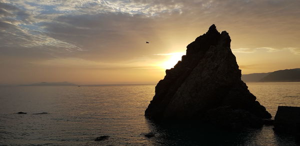 Rock formation in sea against sky during sunset