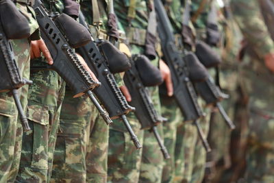 Midsection of army soldiers holding rifles while standing outdoors