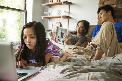 Girl using laptop computer while sitting with parents on bed at home