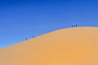 People on sand dune against clear sky