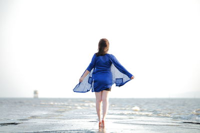 Rear view of woman walking on beach against clear sky