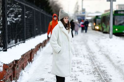 Girl in a fur coat walks along the road traffic of cars. the girl has a knitted hat on her head