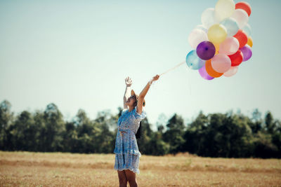 Rear view of woman with balloons on field against clear sky