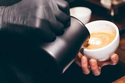 Cropped image of barista adding milk in coffee at shop
