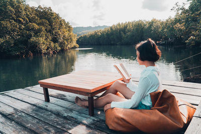 Woman sitting on seat by lake against sky