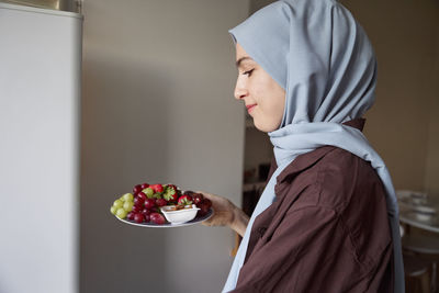 Woman in headscarf carrying plate with fresh fruit at home