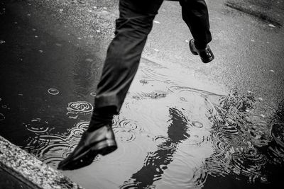 Low section of man jumping over puddle on road during rainy season