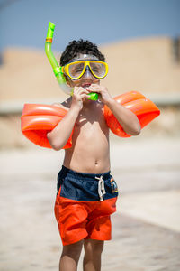 Shirtless boy in swimming goggles and water wings standing outdoors
