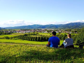 Rear view of friends sitting on grassy field against sky