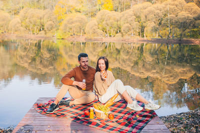 Cheerful couple sitting with dog on pier by lake