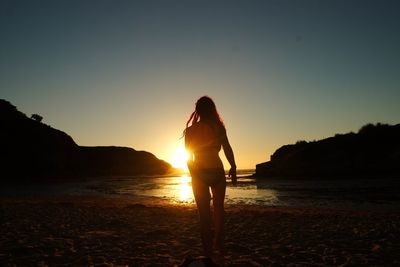 Silhouette woman standing on beach against sky during sunset