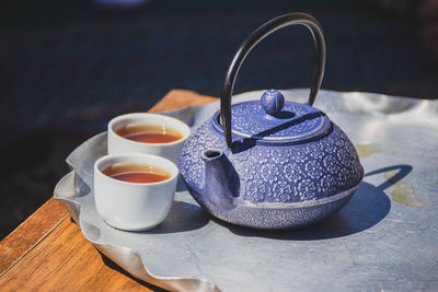 Antique style tea kettle and traditional white tea cups full of hot tea.