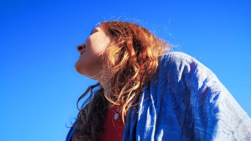 Low angle portrait of young woman against blue sky